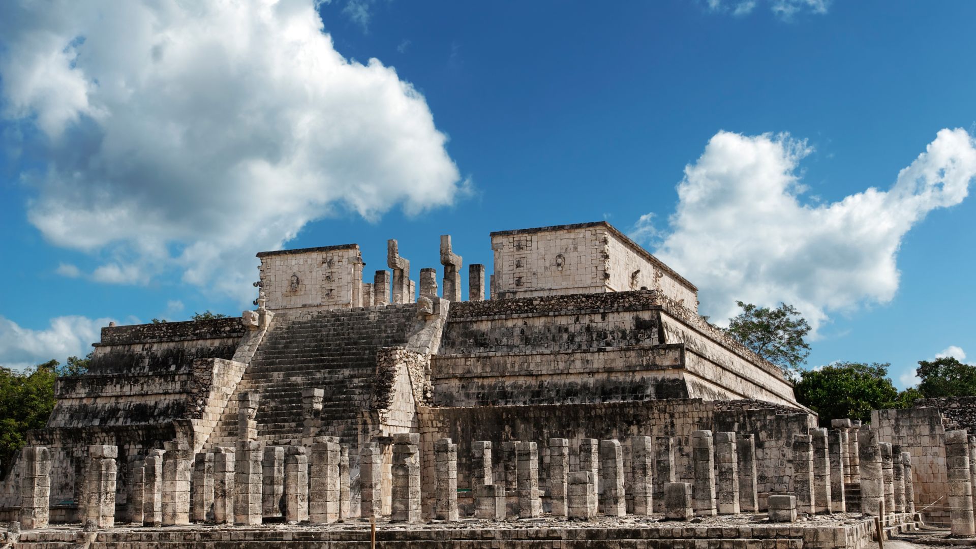 A Stone Building With A Grass Lawn With Chichen Itza In The Background