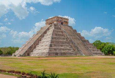 A Large Pyramid With Trees And Grass With Chichen Itza In The Background