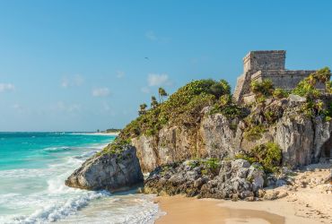 A Castle On A Cliff Above The Ocean With Tulum In The Background