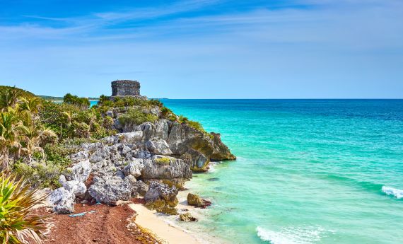 A Rocky Beach With A Castle On It With Tulum In The Background